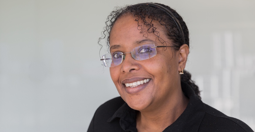 Headshot of a woman in glasses in front of a shiny glass wall.